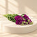 A bouquet of fresh purple stock flowers with green stems and leaves, resting on a white surface.