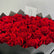 A heart-shaped arrangement of vibrant red roses in a dark gray paper-lined box, with a small white card inserted in the center.