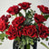 A bouquet of vibrant red roses with green eucalyptus leaves arranged in a dark vase against a plain light background.