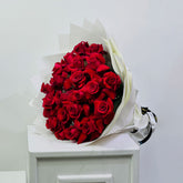 A large bouquet of red roses wrapped in white paper, displayed on a white cabinet against a plain light gray wall. flower delivery in qatar