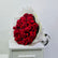 A large bouquet of red roses wrapped in white paper, displayed on a white cabinet against a plain light gray wall. flower delivery in qatar
