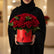 A large bouquet of red roses with green leaves arranged in a bright red cylindrical box with butterfly cutouts and a black base, displayed on a white surface against a light gray background.