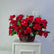A large arrangement of vibrant red roses and green foliage in a brown wicker basket, displayed on a white cabinet against a light gray wall.