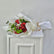 A bouquet of red roses wrapped in white paper with a white bow and ribbon, placed on a white cabinet against a light gray wall.