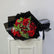 A bouquet of red roses wrapped in black paper, placed on top of a white cabinet against a plain light gray wall.