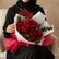A bouquet of red roses wrapped in white and bright pink patterned paper, tied with a matching bow, displayed on a white pedestal against a light gray background.