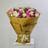 A large bouquet of pink, cream, and purple flowers wrapped in brown kraft paper and tied with a cream ribbon, displayed on a white pedestal against a light gray background.