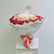 A large bouquet of roses wrapped in white tissue paper and tied with a red and white ribbon, displayed on a white pedestal against a plain light gray background.