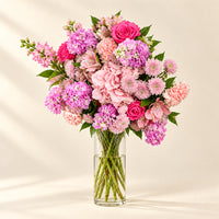 A bouquet of pink and magenta flowers wrapped in brown kraft paper, placed on a white marble countertop with a matching brown paper bag behind it.