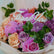 A close-up of a floral bouquet with peach roses, pink and purple flowers, green eucalyptus leaves, and a white script 'Thank You' sign placed on top.