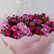 A vibrant bouquet of pink and purple roses with green foliage, wrapped in light pink tissue paper. A small card with the brand name 'VIVA FLORA' is visible at the top.