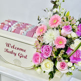 A baby shower favor box with a floral arrangement. The box is cream-colored with 'Welcome Baby Girl' printed on the front.
