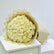 A large bouquet of cream-colored roses wrapped in sheer beige tissue paper, displayed on a white pedestal against a light gray background.