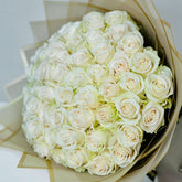 A large round bouquet of white roses wrapped in beige tissue paper, photographed from above on a light neutral background.