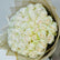 A large round bouquet of white roses wrapped in beige tissue paper, photographed from above on a light neutral background.
