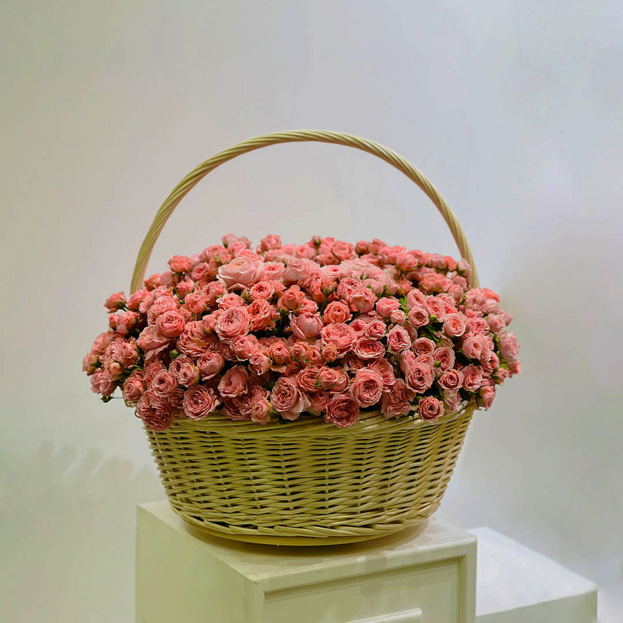 Basket filled with soft pink spray roses arranged in a rounded floral display