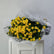A bouquet of yellow roses wrapped in white newspaper-patterned paper, displayed on a white cabinet against a light gray wall.
