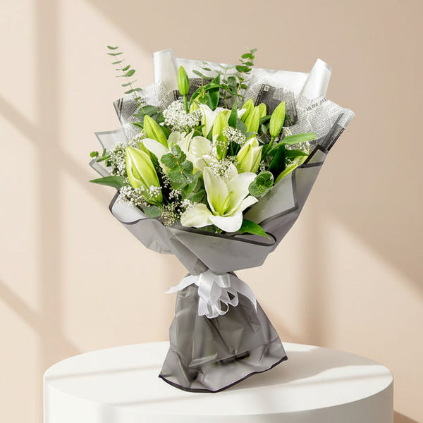 A hand bouquet of white lilies and eucalyptus leaves wrapped in black plastic paper with a white ribbon.