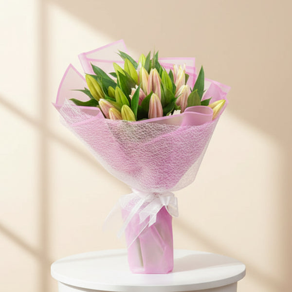 A fresh flower bouquet consisting of pink and green Stargazer lilies, wrapped in pink paper with a white ribbon.